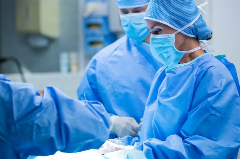 A surgeon's face behind a surgical mask and other doctors performing a procedures
